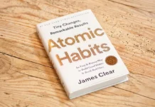 Atomic Habits (2018): The Self-Help Cult Classic That Wants to Fix You One Microscopic Habit at a Time image of book on wood surface atomic habits (2018) by james clear
